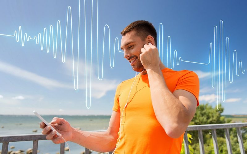 fitness-sport-people-technology-healthy-lifestyle-concept-smiling-young-man-with-smartphone-earphones-listening-music-summer-seaside-sound-wave-signal-diagram-min